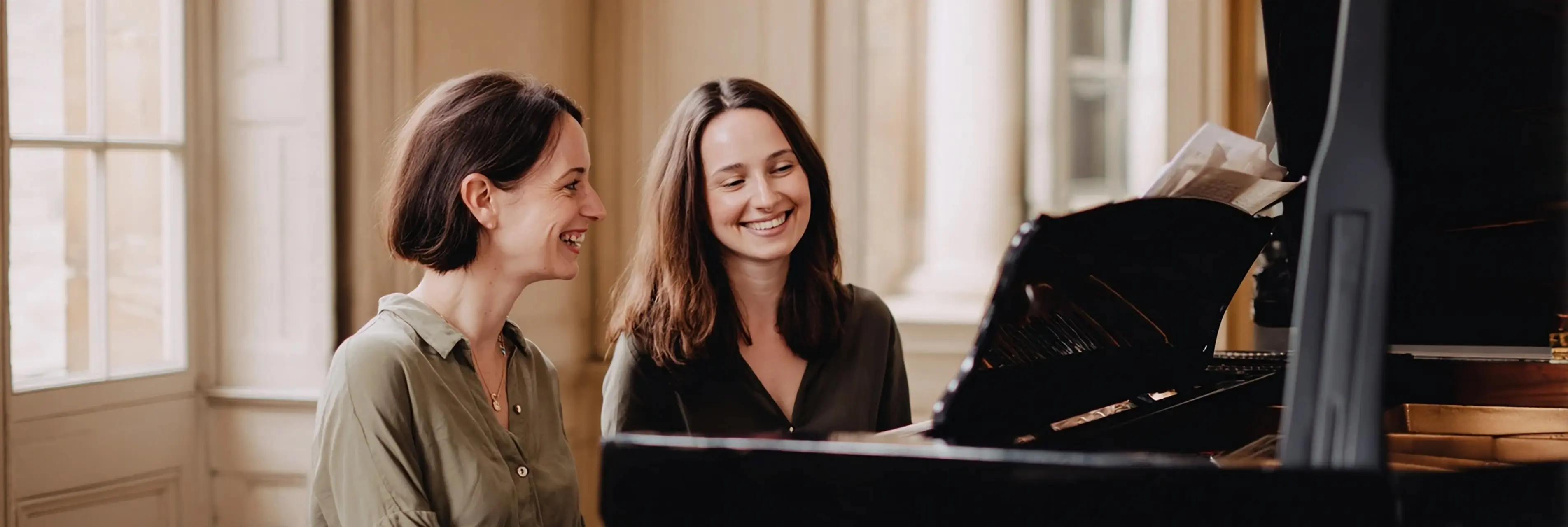 A piano teacher and an adult student smiling together at a grand piano