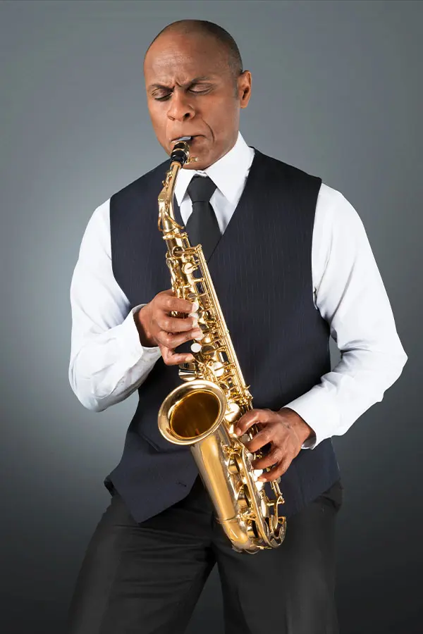 Bald man in a dark waistcoat playing alto saxophone