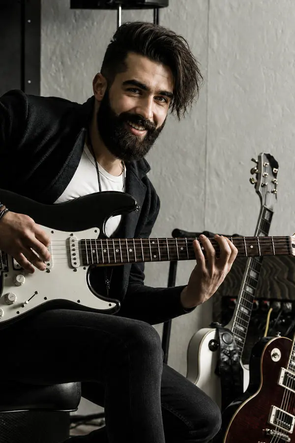 Bearded man smiling while playing an electric guitar