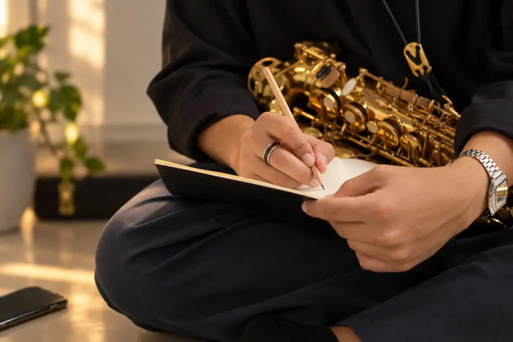 Seated saxophonist writing in a notebook with a saxophone in their lap