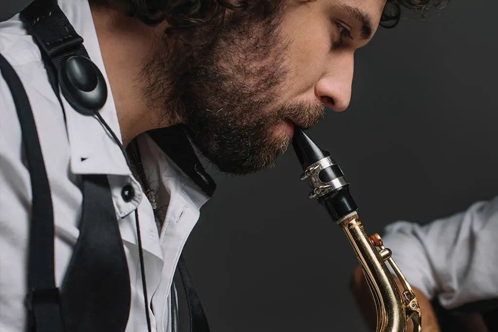 Curly-haired bearded man playing a saxophone in close-up