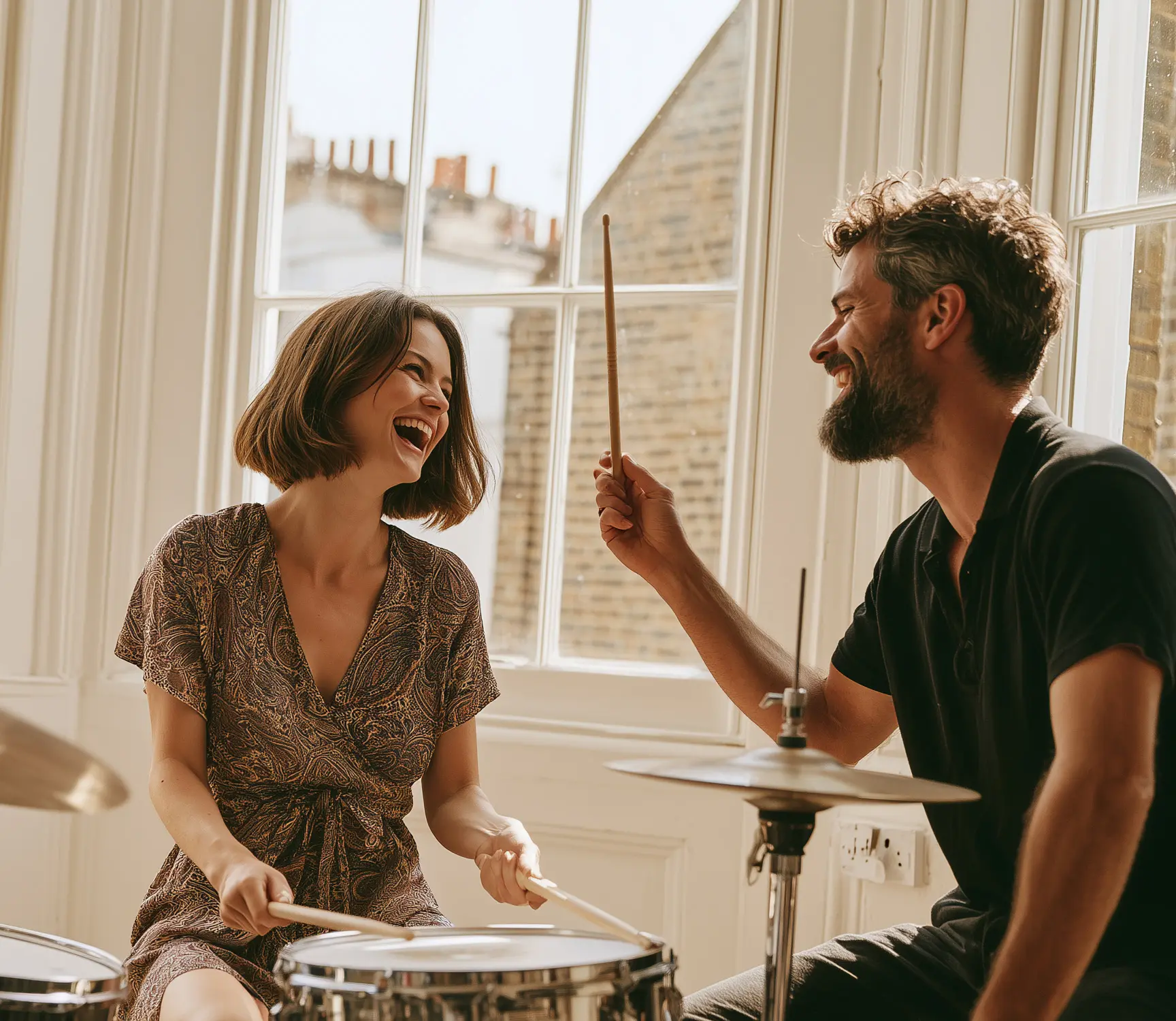 Drum student laughing at the kit as her teacher holds up a drumstick to show the grip.