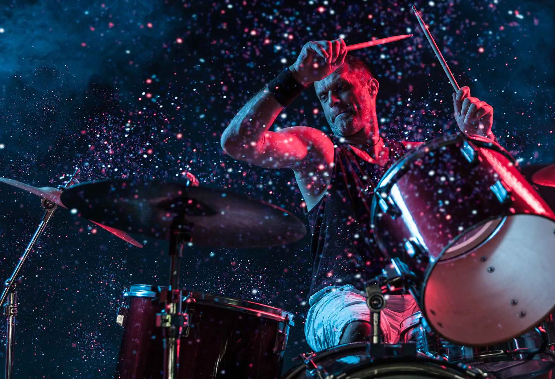 Drummer playing a drum kit under dramatic stage lighting