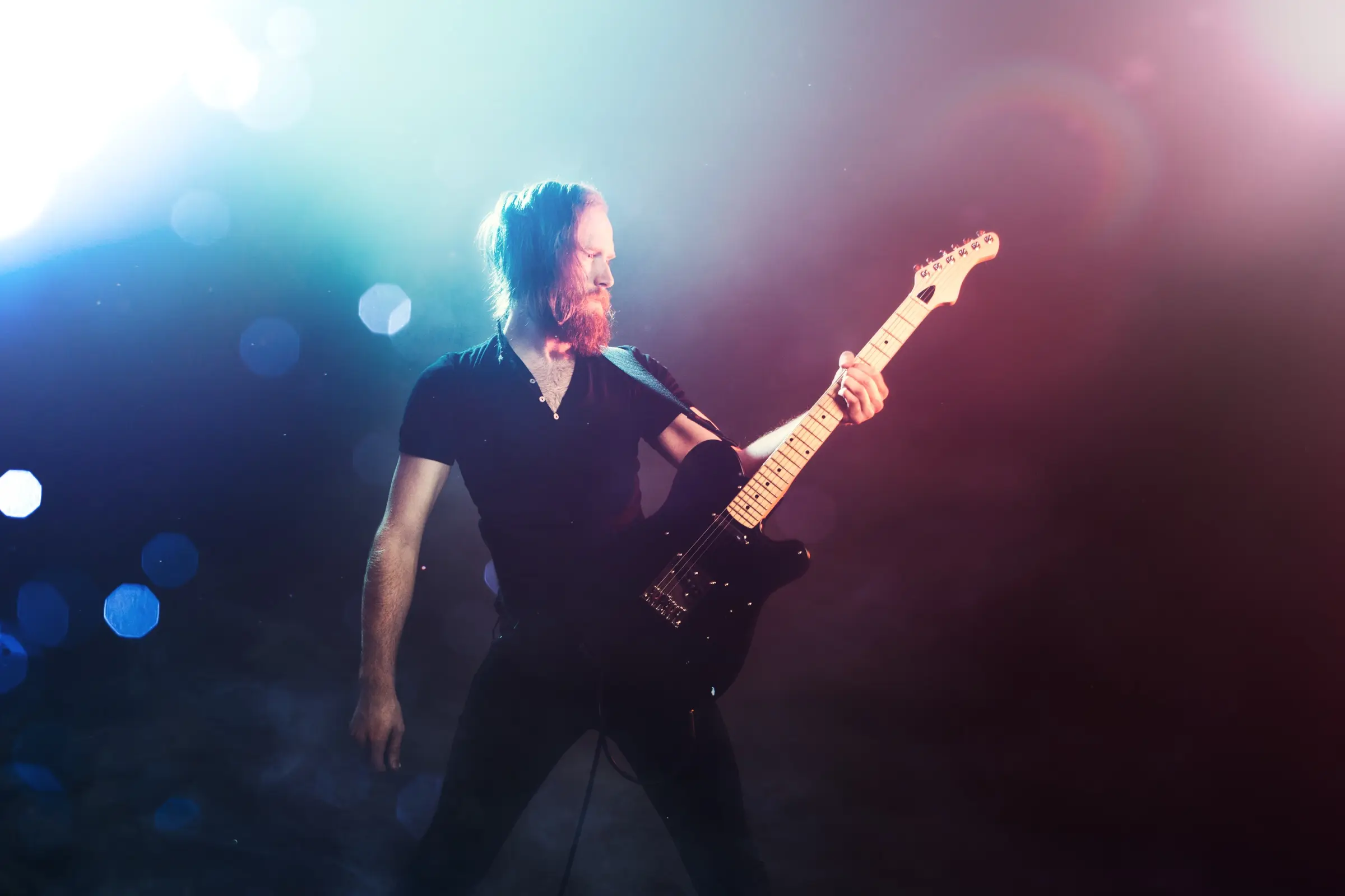 Electric guitarist performing on stage under coloured lights.