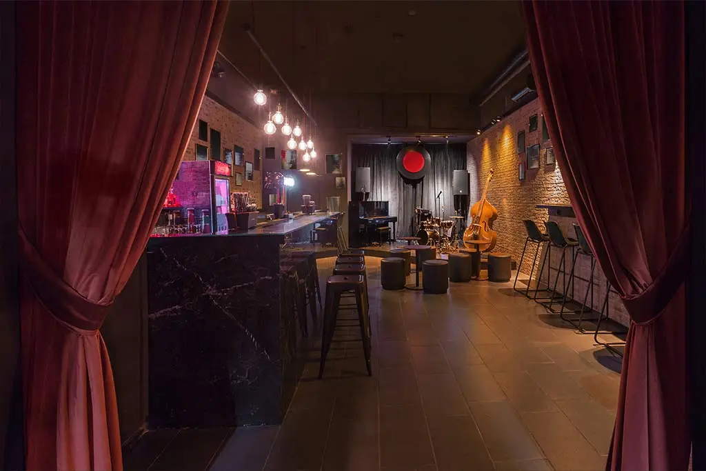 Empty bar with red curtains, stools and a double bass on stage