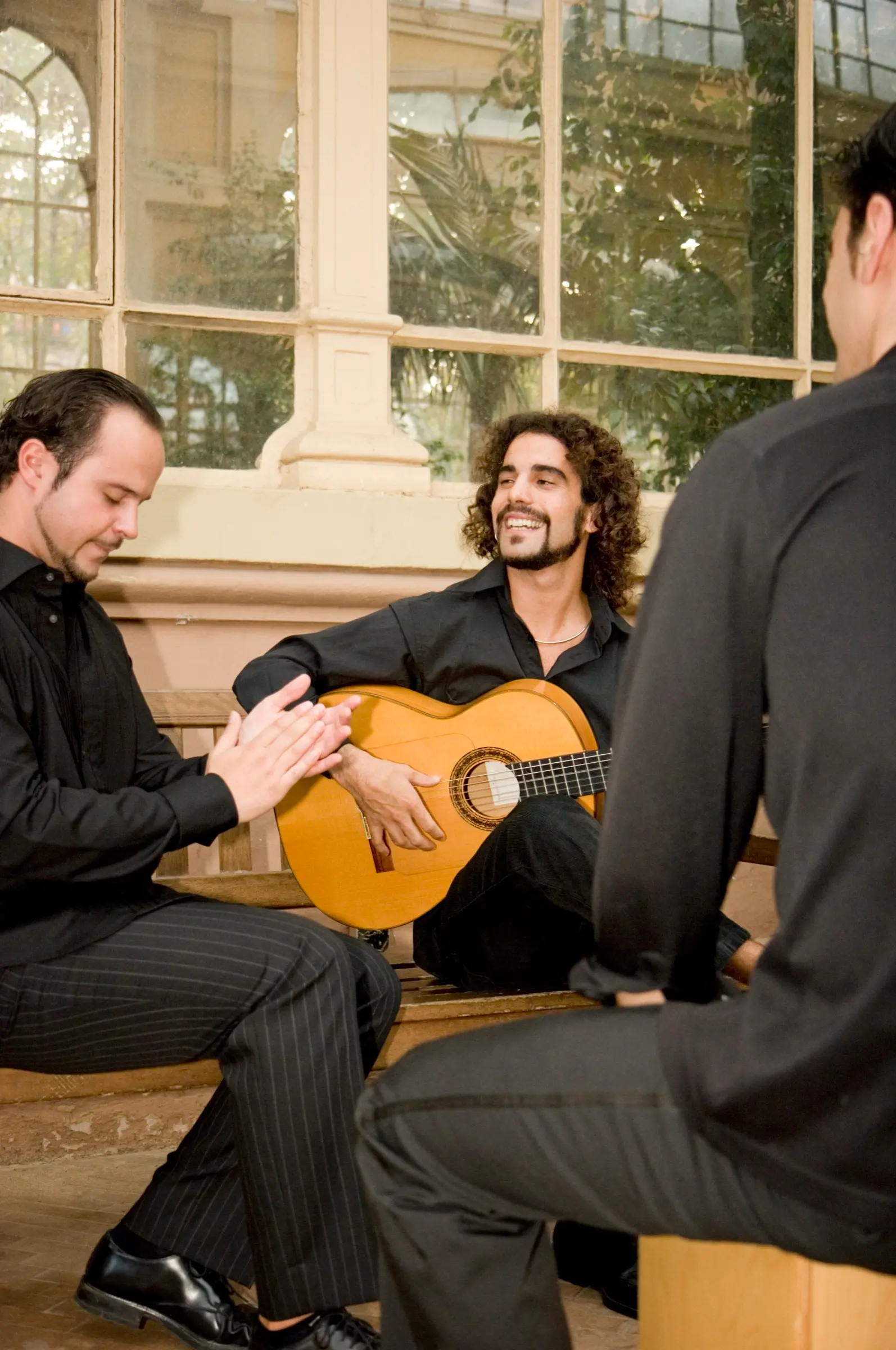 Guitarist playing flamenco with two fellow musicians.
