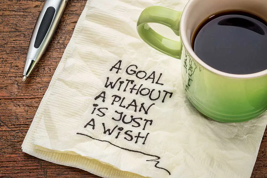Handwritten goal quote on a napkin beside a coffee mug and pen