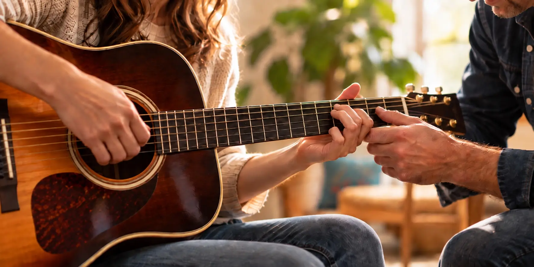 Guitar teacher guiding a student’s hand on the fretboard in warm sunlight