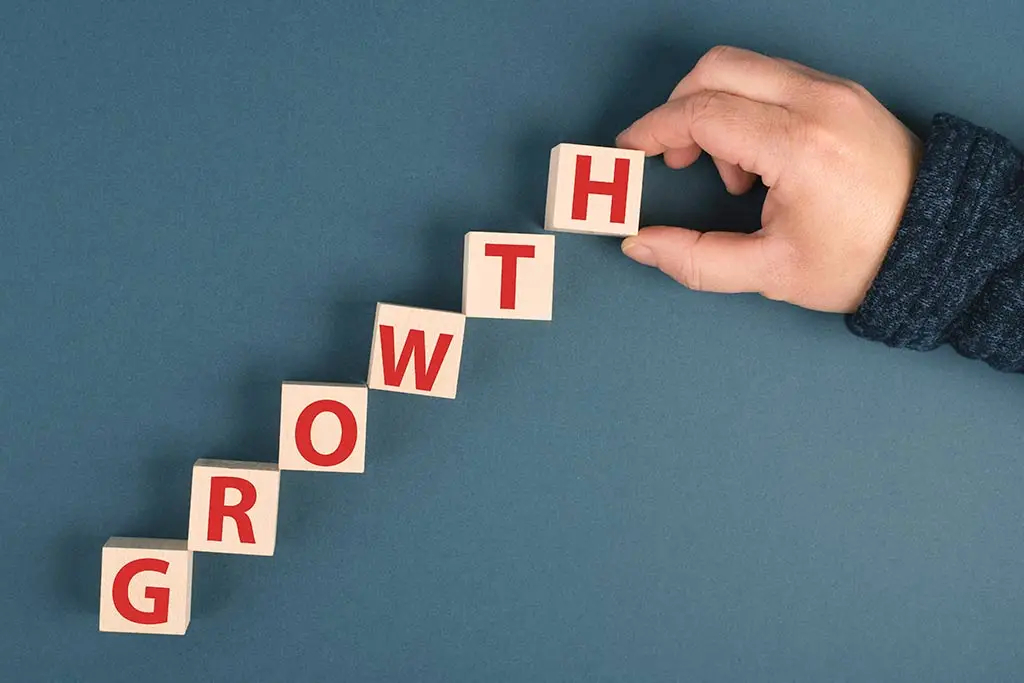 Hand arranging letter blocks spelling growth in a staircase