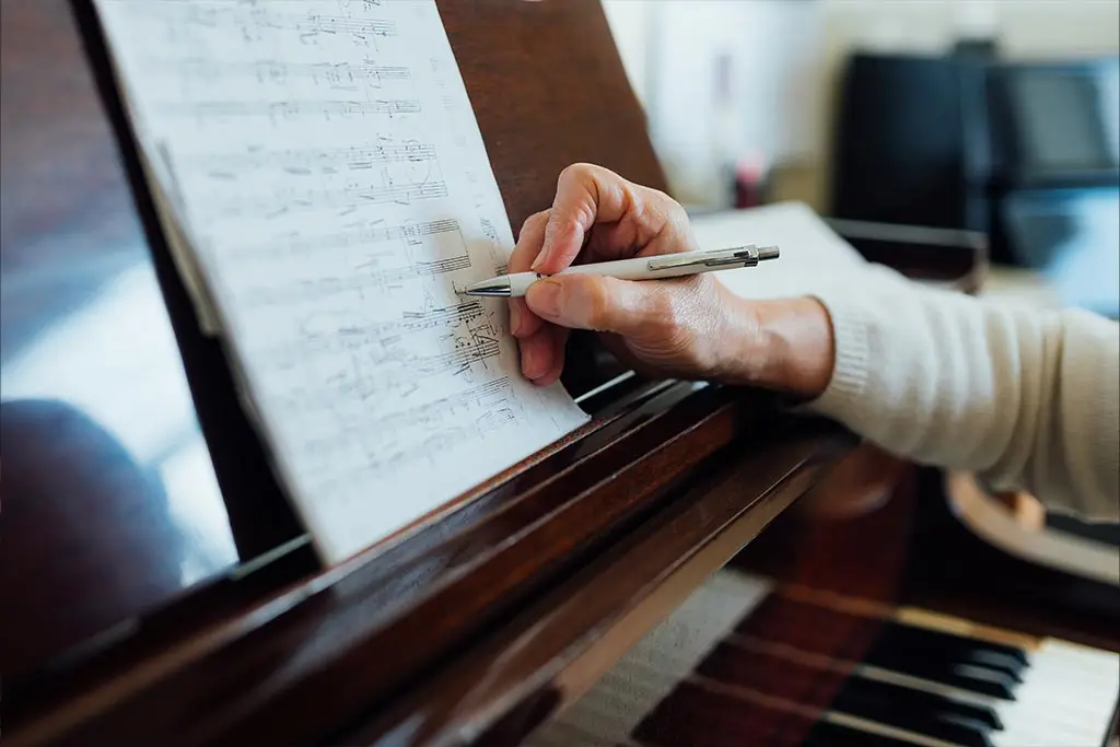 Hand marking sheet music with a pen at a piano