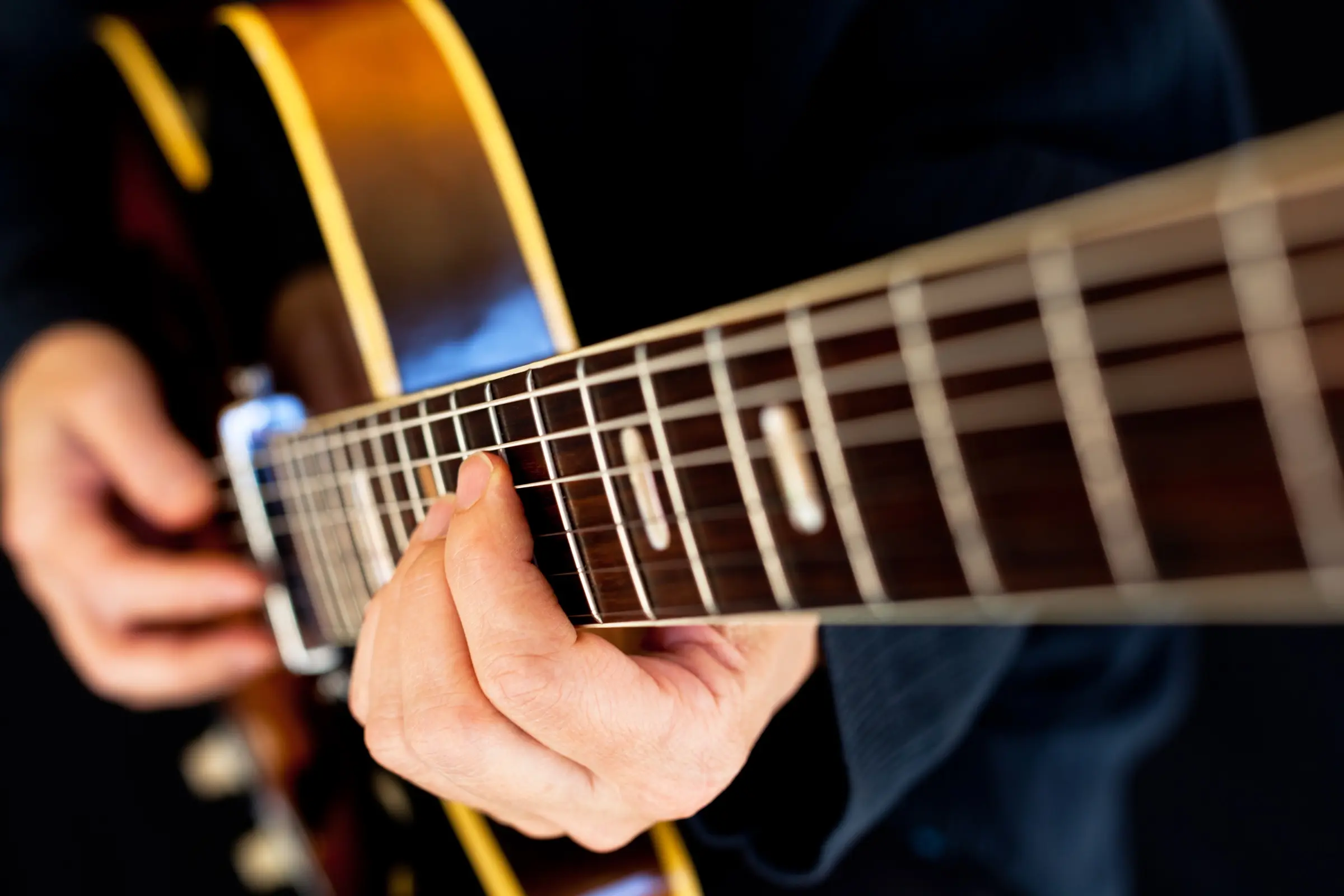 Close-up of a hand on the neck of a vintage archtop guitar.
