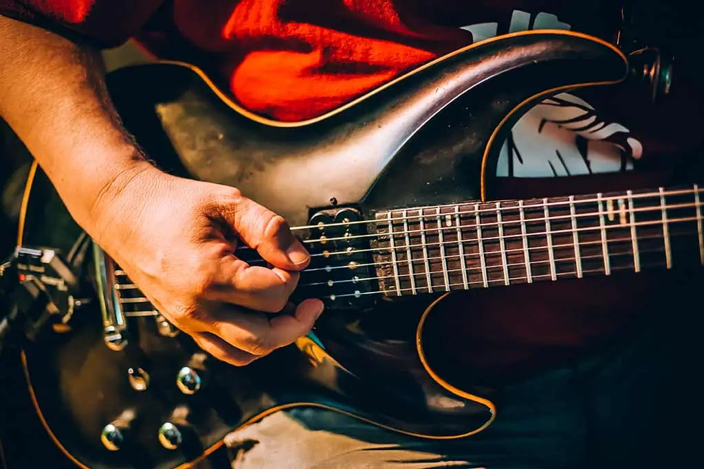Hand picking the strings of a black electric guitar