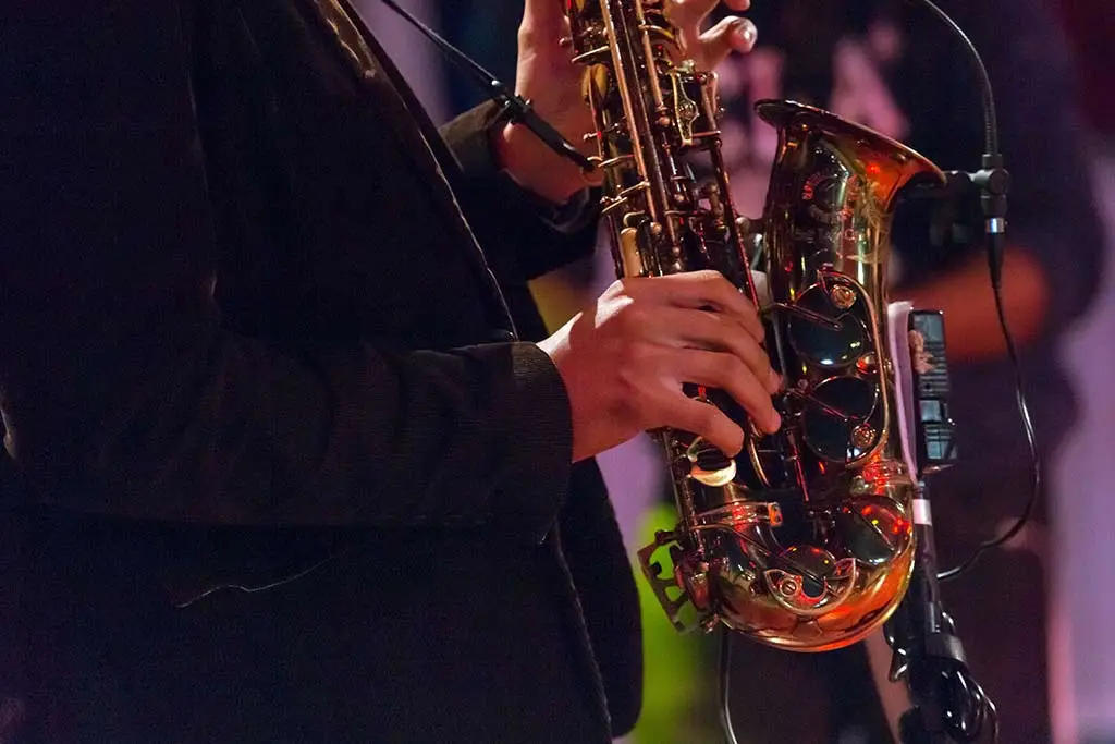 Hands fingering a saxophone beside a microphone