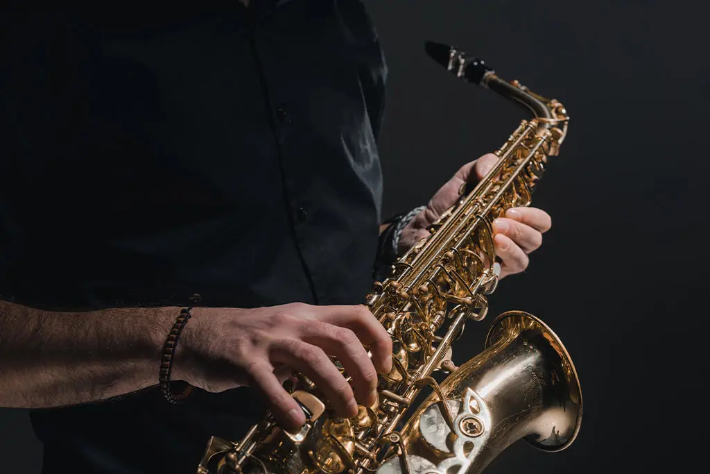 Hands holding a saxophone sideways against a dark background