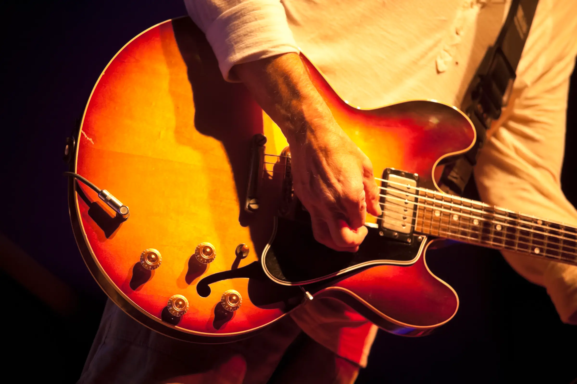 Close-up of hands playing a sunburst semi-hollow electric guitar.
