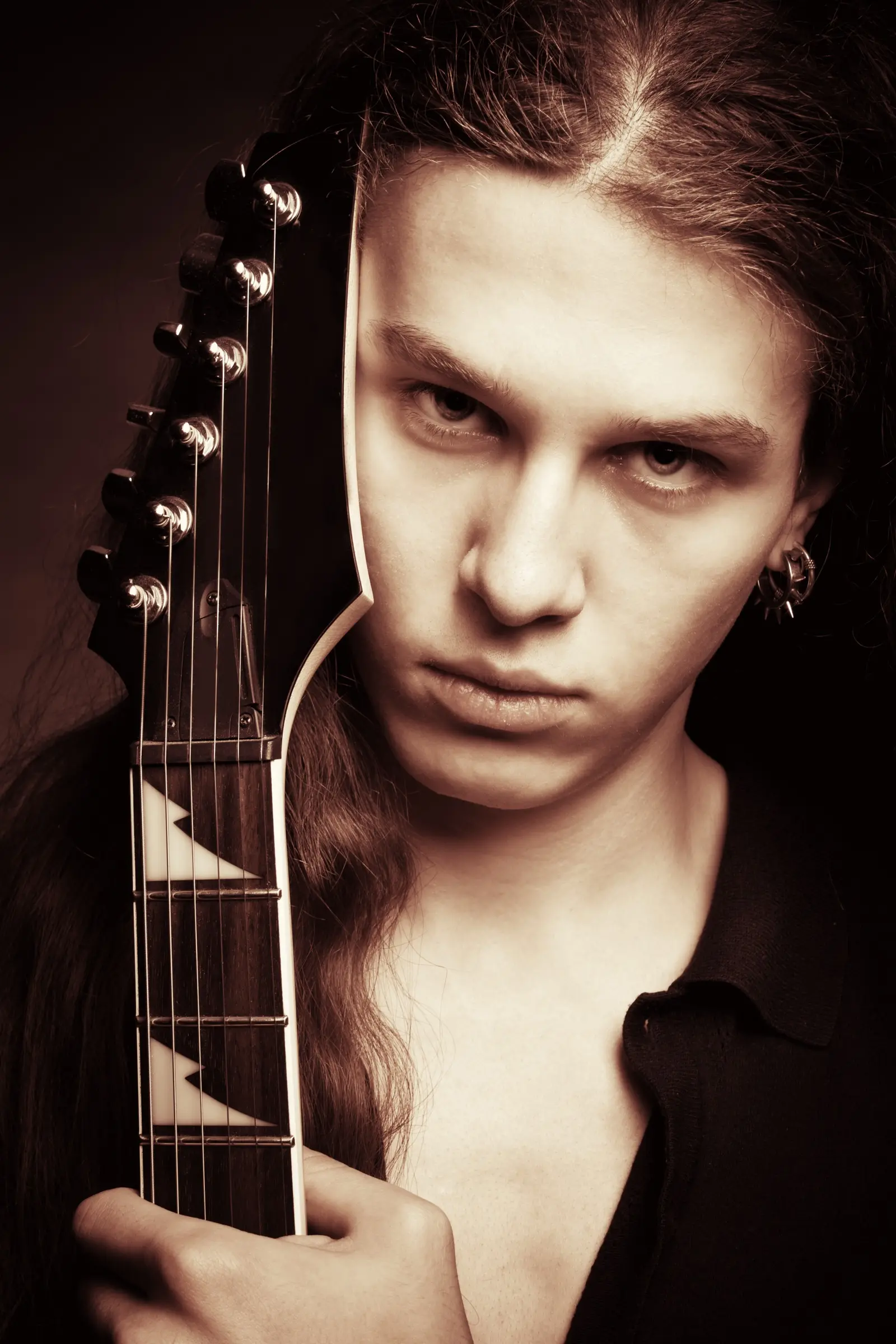Long-haired young man holding the neck of an electric guitar.