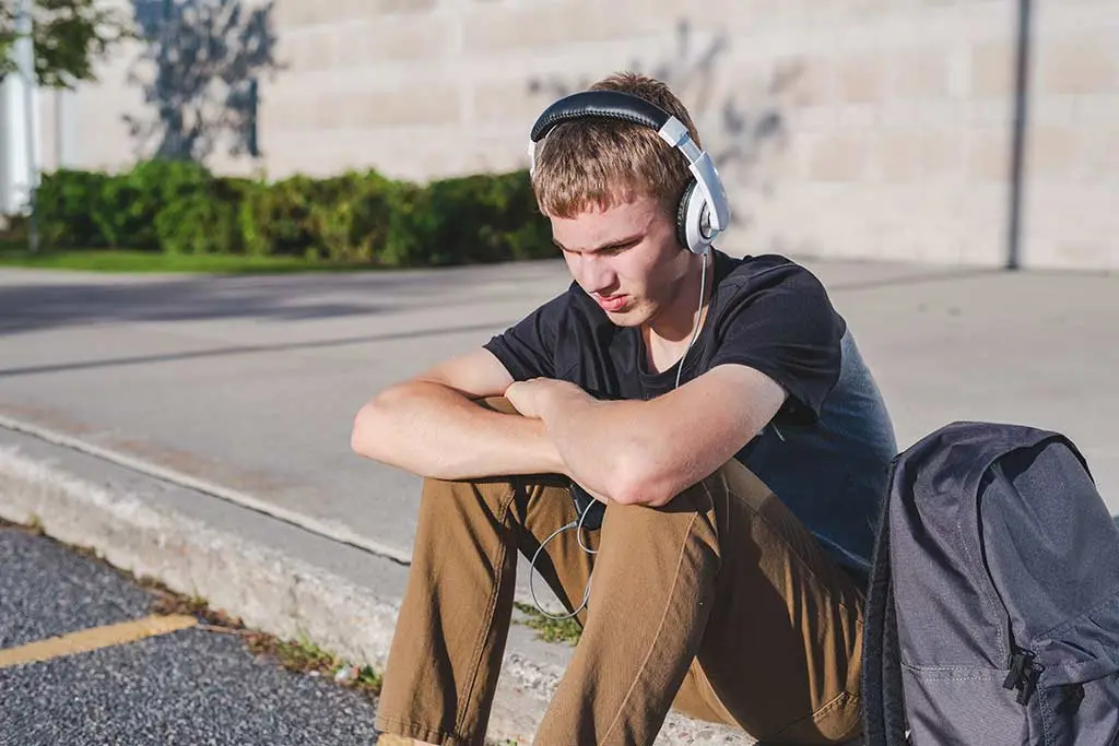 Male teenager sitting on curb listening to music