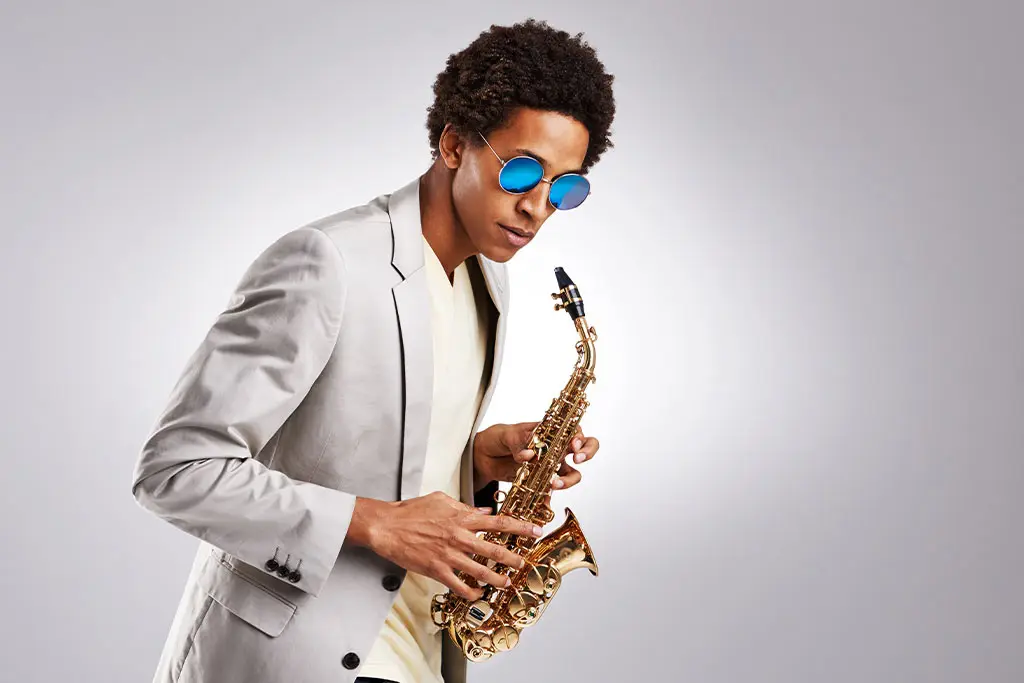 Man in blue sunglasses and white blazer holding an alto saxophone