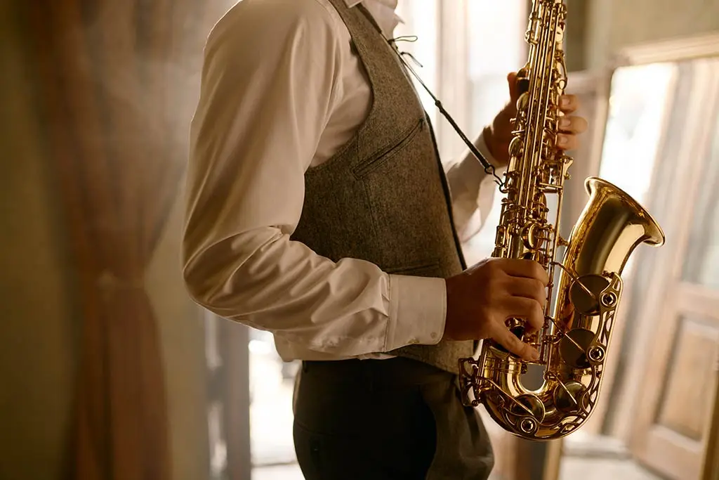 Man in a waistcoat holding a saxophone by a window