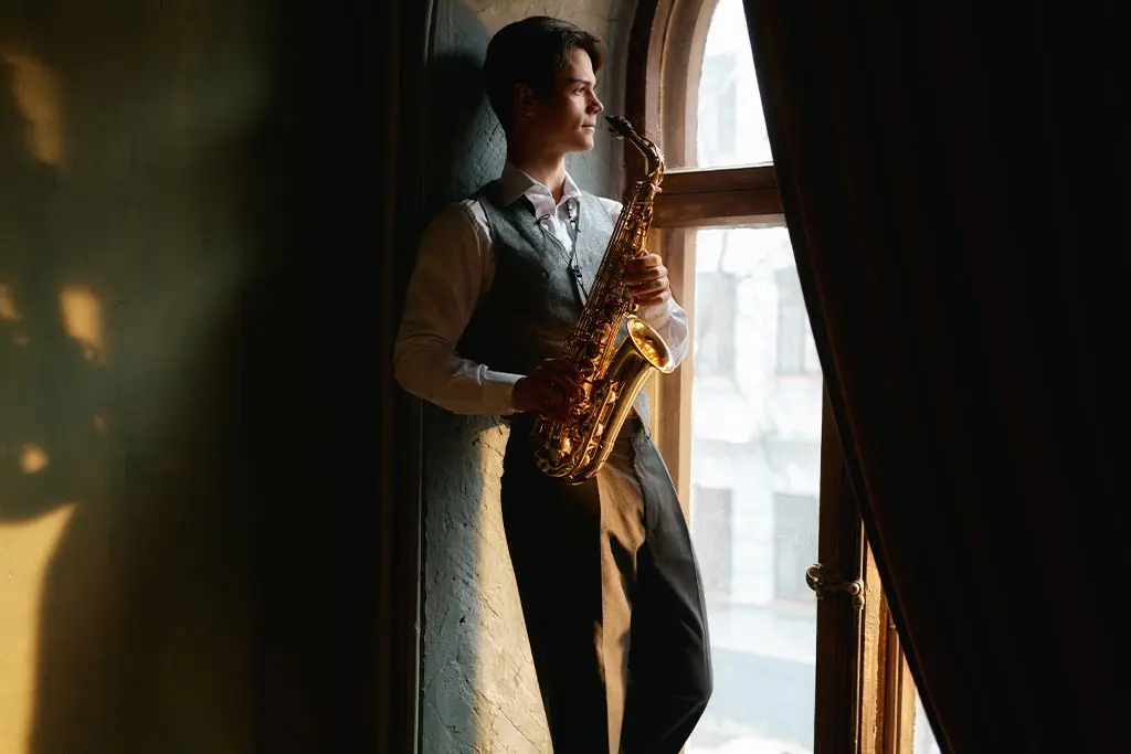 Man holding a saxophone beside a window