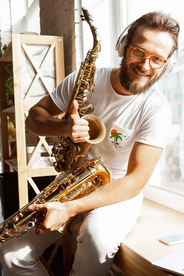 Man sitting by a window holding two saxophones