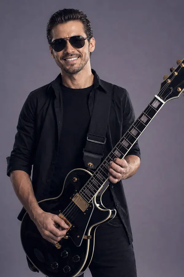 Man in sunglasses and a black shirt playing a black electric guitar