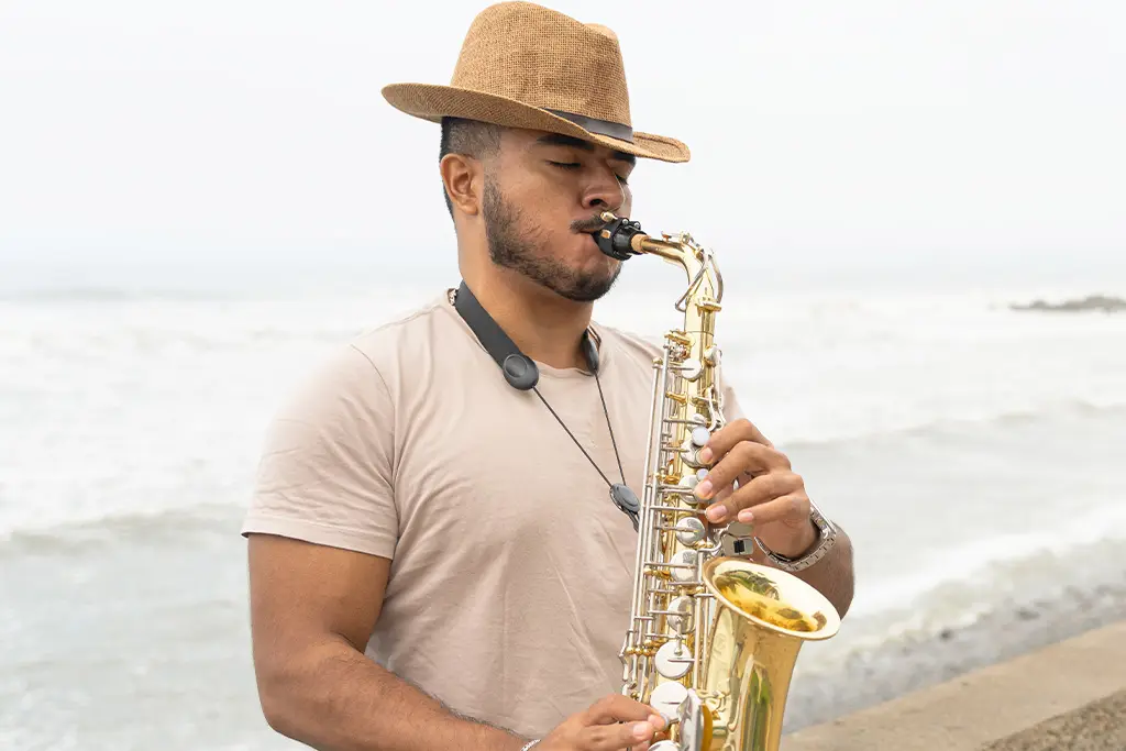 Man in a hat playing alto saxophone by the sea