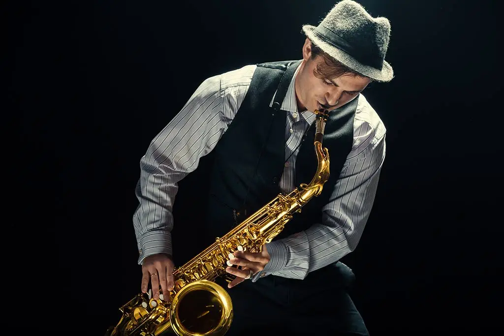 Man in a hat playing a saxophone against a dark background