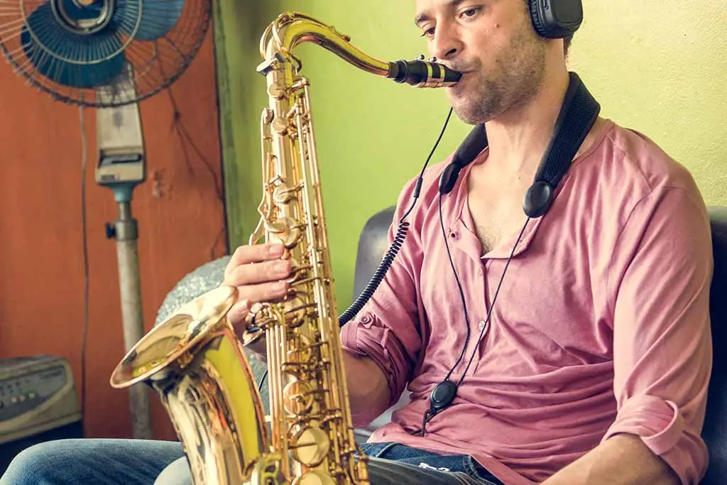 Man in a pink shirt wearing headphones and playing tenor saxophone