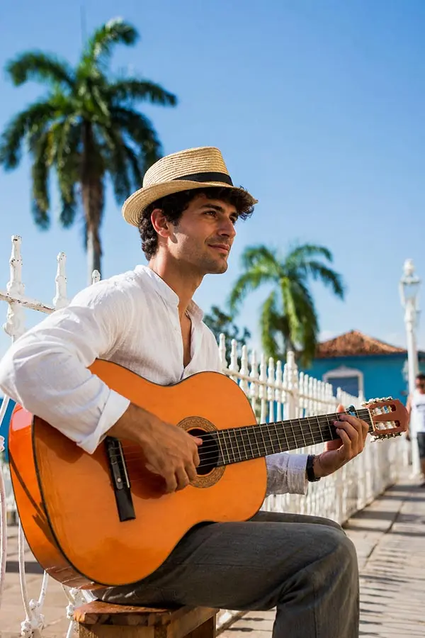 Man in a straw hat playing classical guitar by palm trees