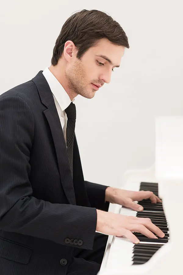 Man in a suit playing a white piano