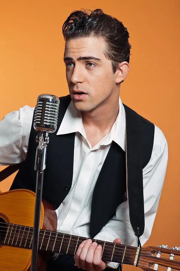 Man singing into a vintage microphone while playing an acoustic guitar