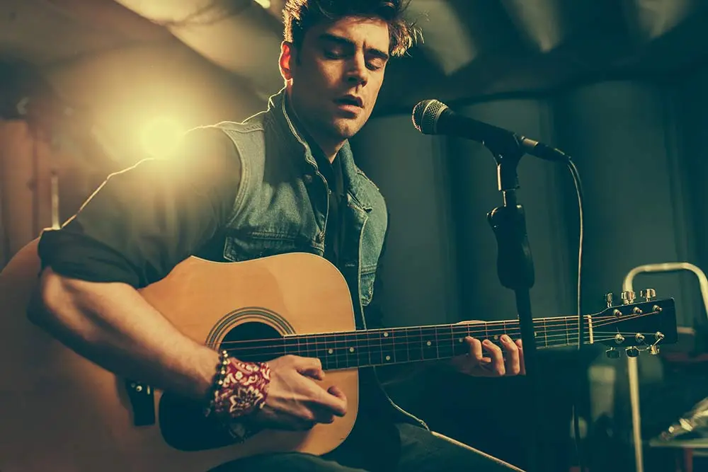 Man playing acoustic guitar beside a stage microphone