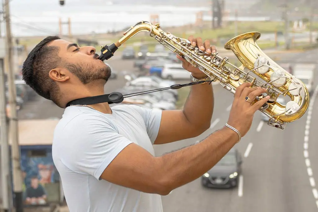Man raising an alto saxophone above a road with traffic