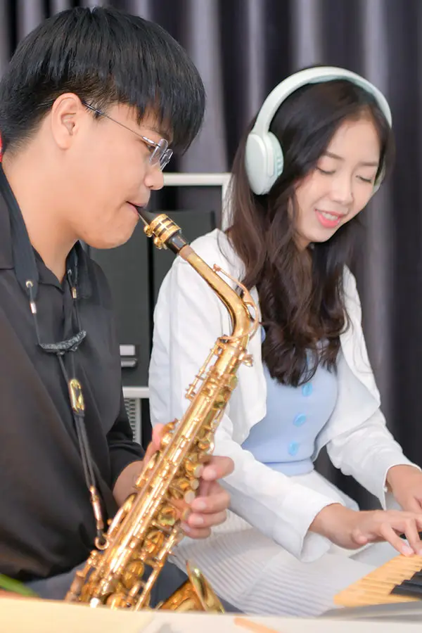 Man playing alto saxophone beside a woman wearing headphones at a keyboard