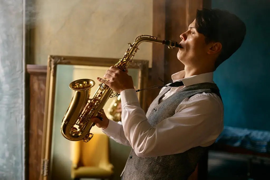 Man in a grey waistcoat playing alto saxophone beside a mirror
