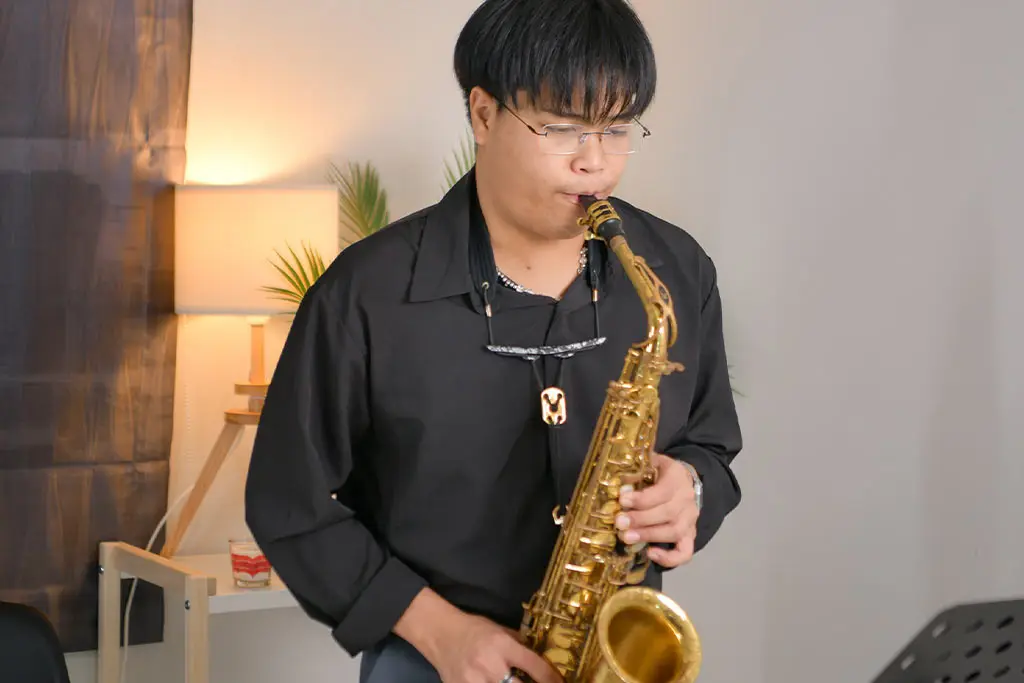 Man in a black shirt playing alto saxophone near a lamp