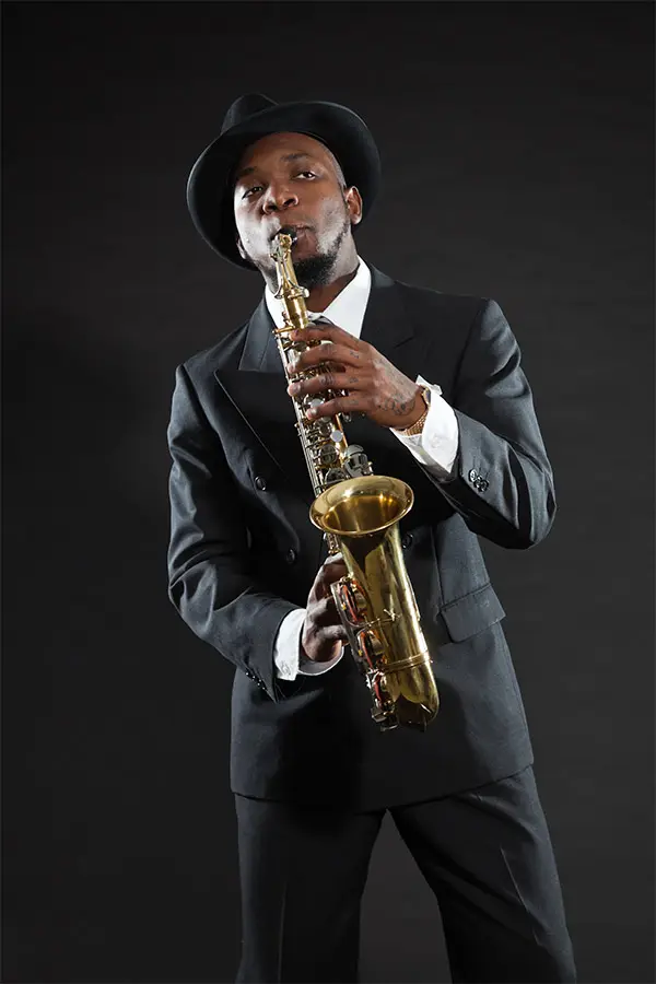 Man in a black suit and hat playing alto saxophone
