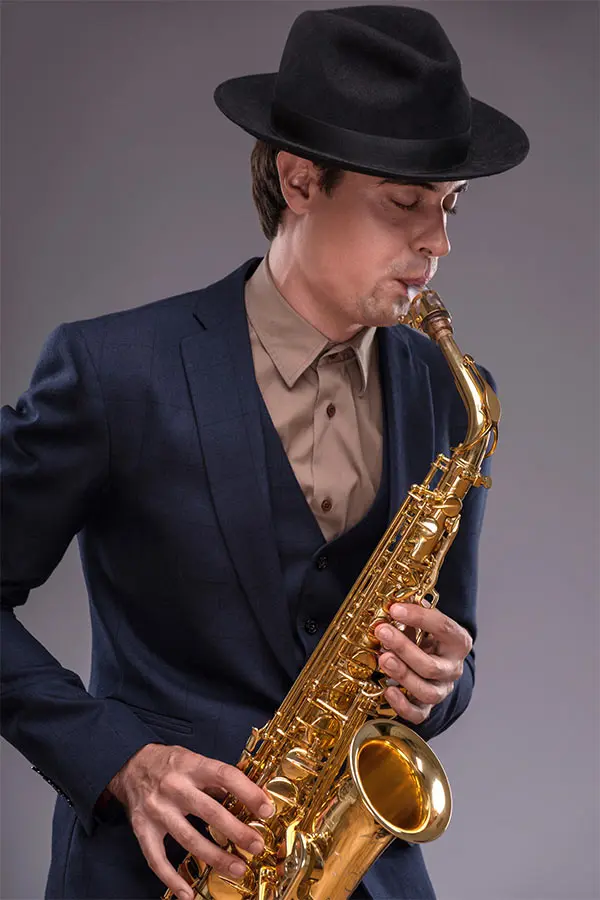 Man in a blue suit and black hat playing alto saxophone