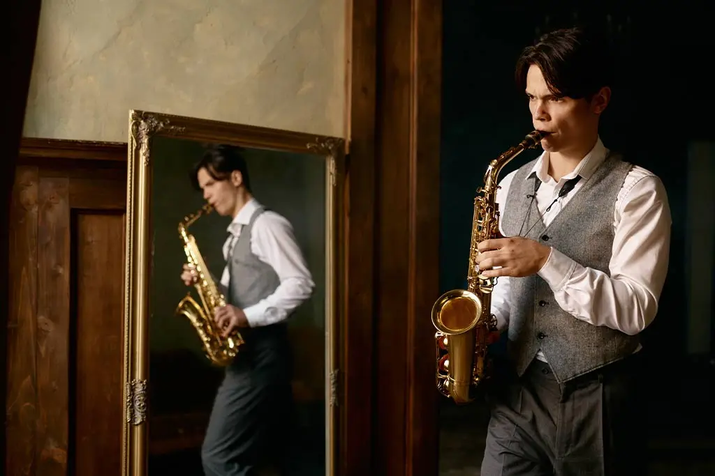 Man playing alto saxophone beside a large mirror