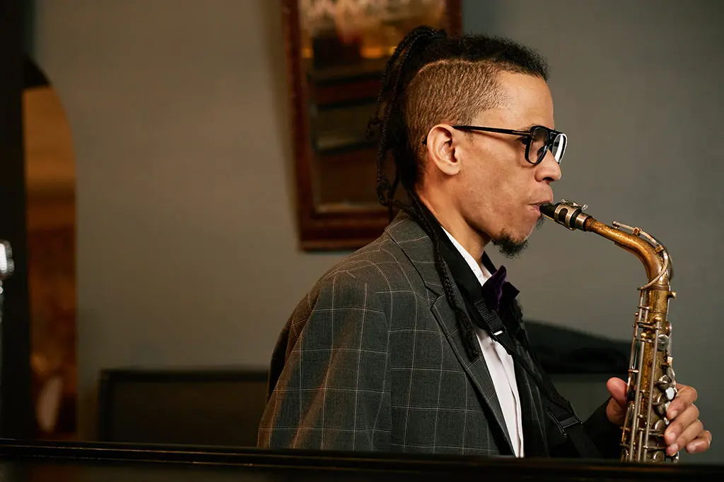 Man with glasses playing alto saxophone in a checked jacket