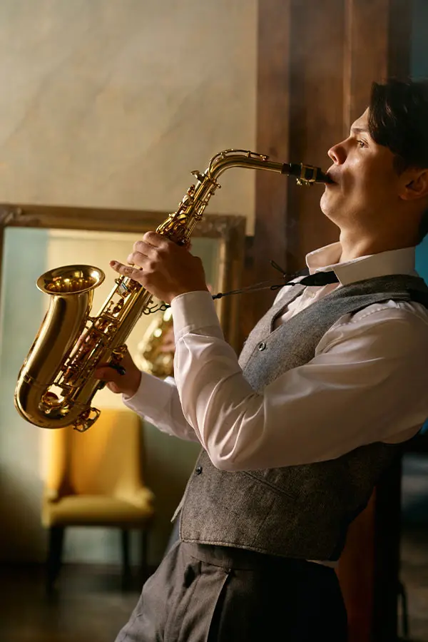 Man in a grey waistcoat playing alto saxophone indoors