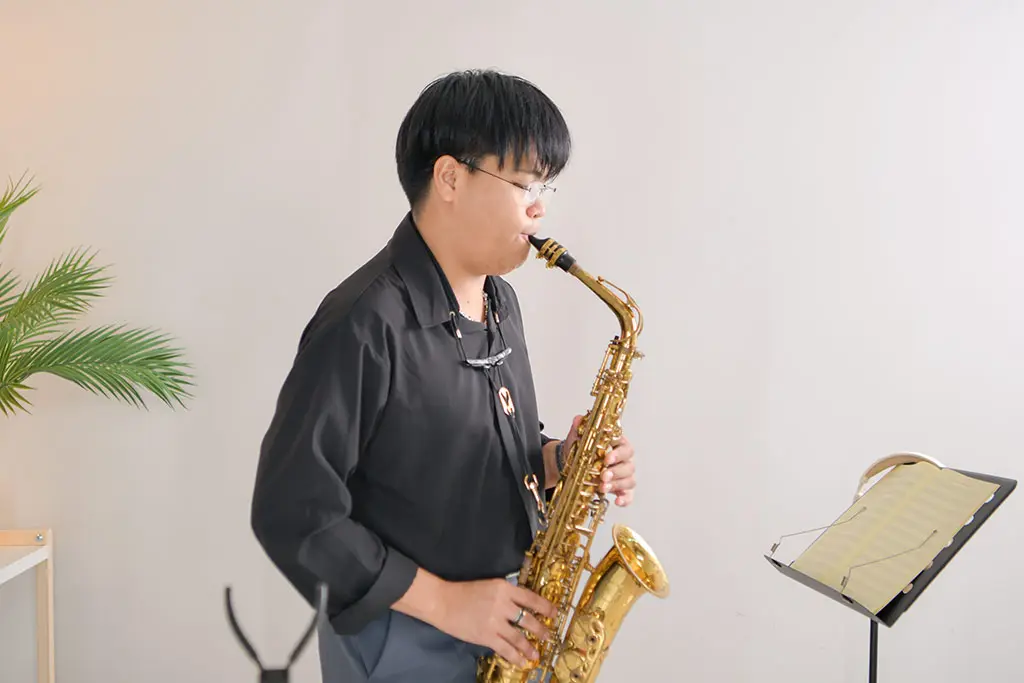 Man in a black shirt playing alto saxophone beside sheet music