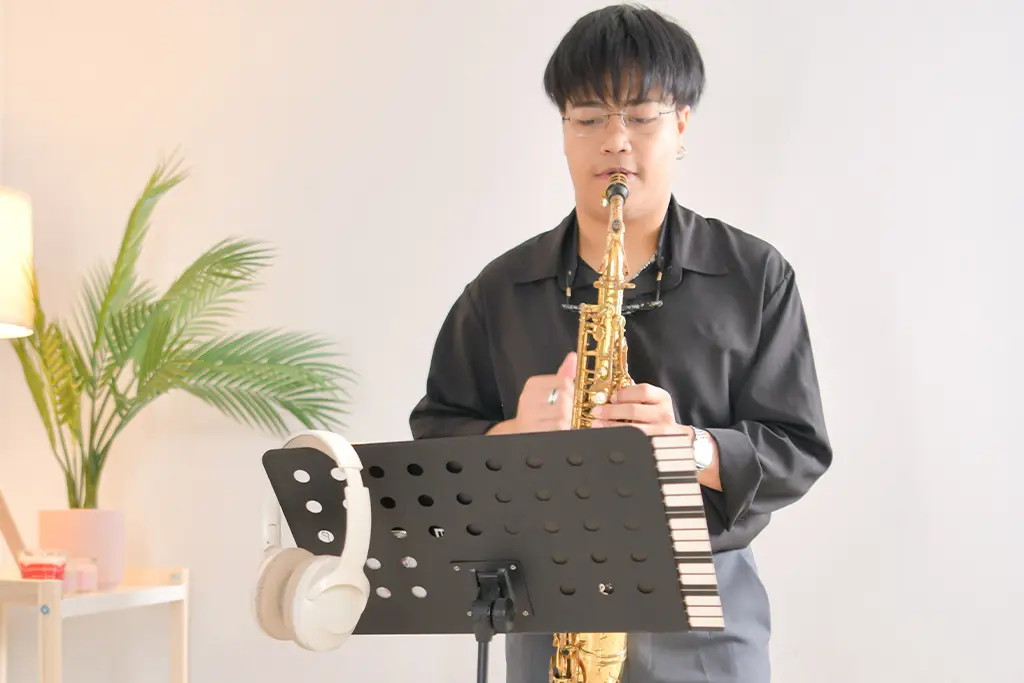 Man playing alto saxophone behind a stand with headphones hanging