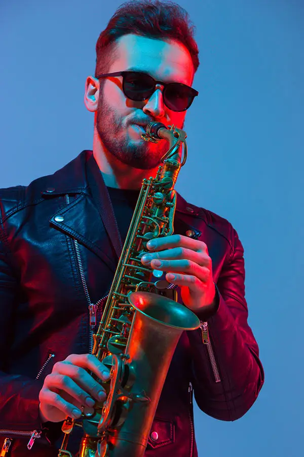 Man in sunglasses playing alto saxophone under blue and red lighting