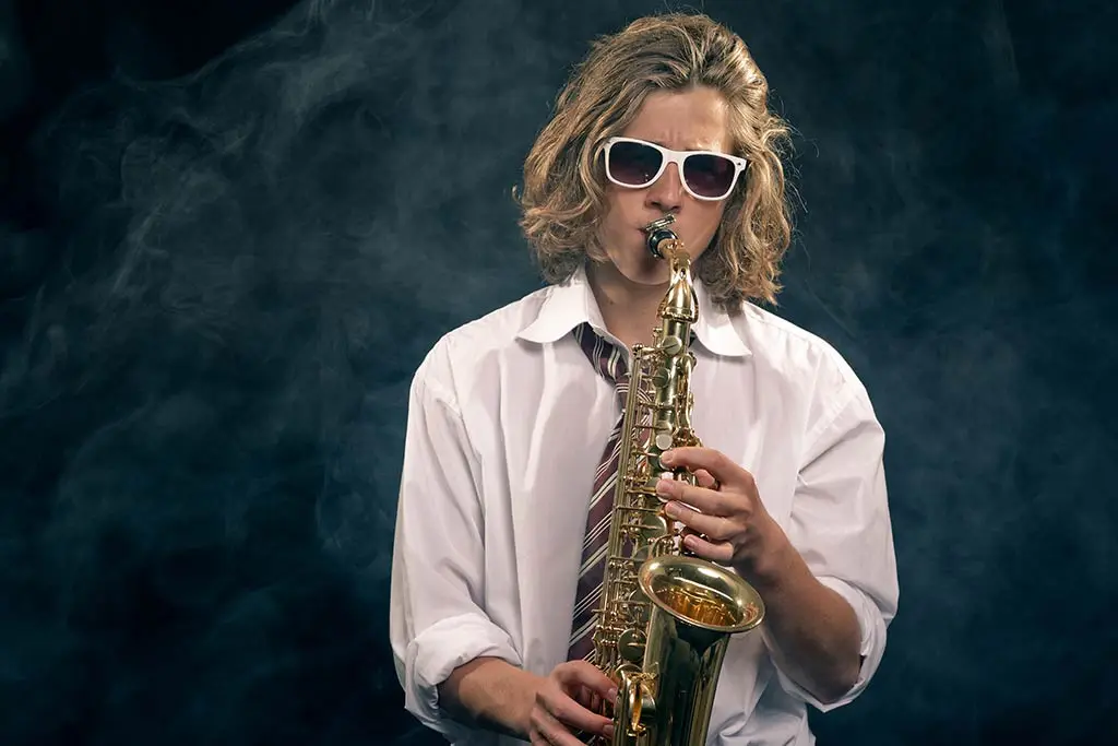 Man in white sunglasses playing alto saxophone in smoky light