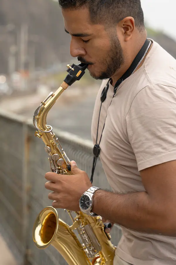 Man playing alto saxophone beside a waterfront railing
