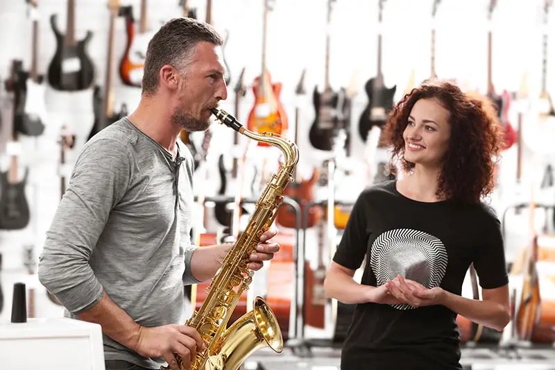 Man playing alto saxophone while a woman watches among guitars