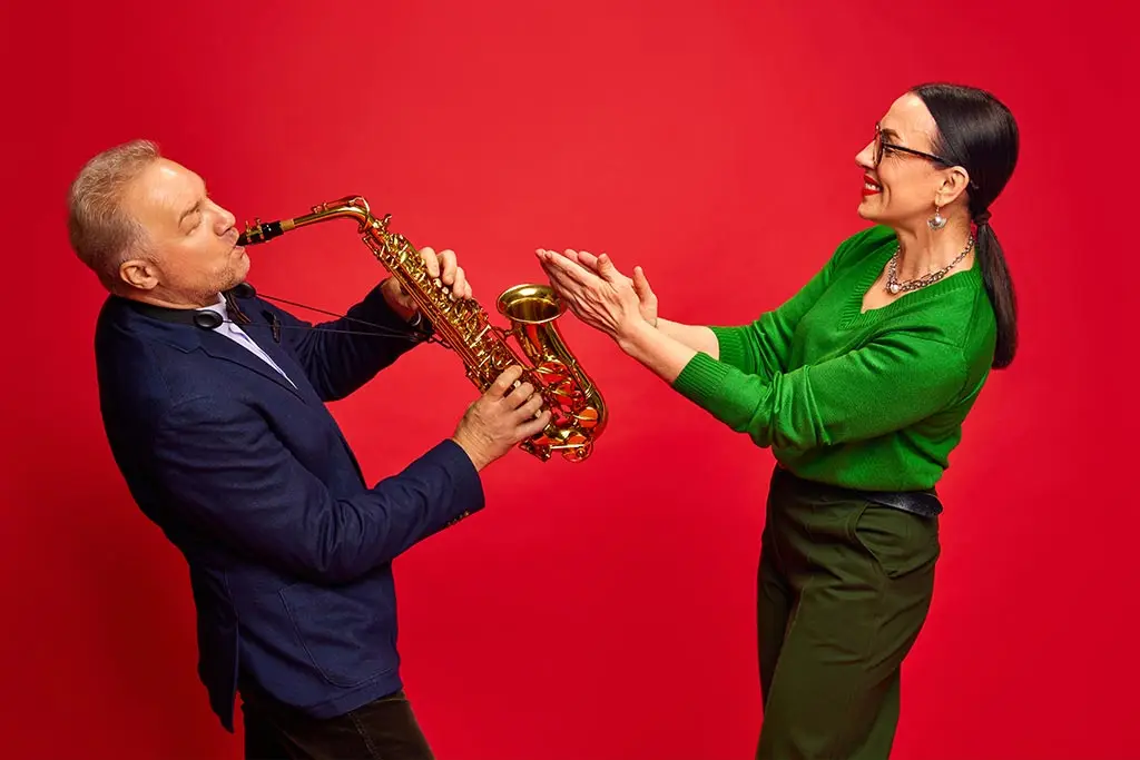 Man playing an alto saxophone while a woman claps beside him