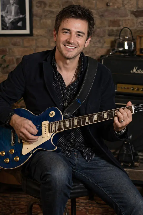 Smiling man seated with a blue electric guitar